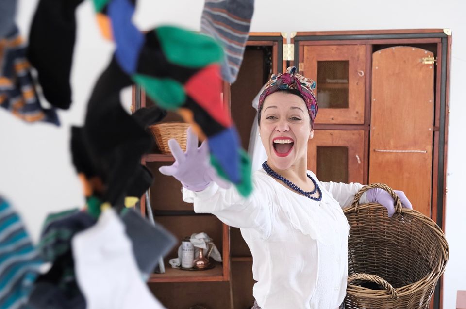 Miss Baines, a woman from the 1950s holds a washing basket full of socks which she is throwing towards the camera